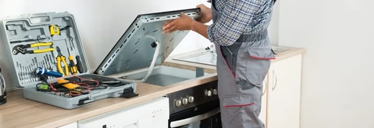 Cooktop repair technician lifting a built-in stovetop for service in Anaheim, CA